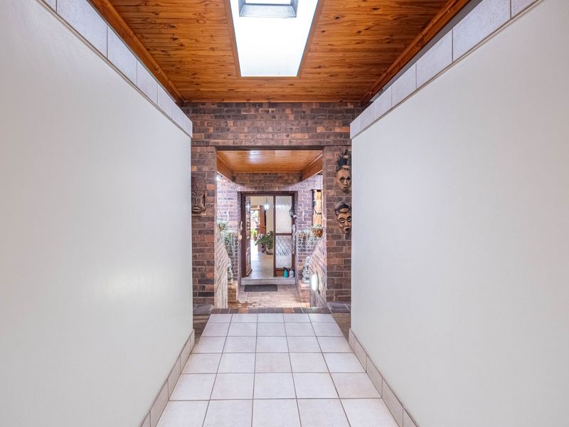 A bright entrance hallway featuring exposed brick walls, a timber ceiling with a central skylight, and neutral tiled flooring leading to the main living area.