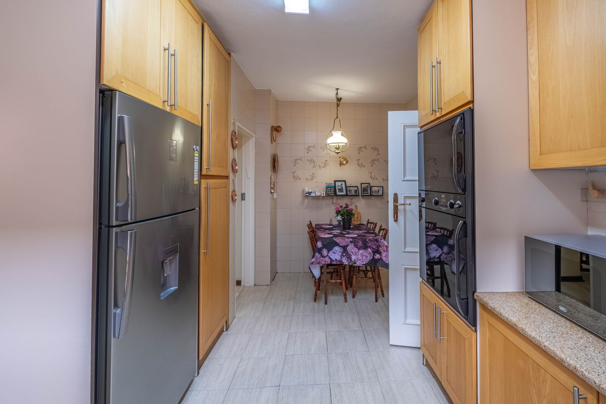 A functional kitchen featuring light wood cabinetry, built-in oven, and tiled flooring, leading into a dining area.
