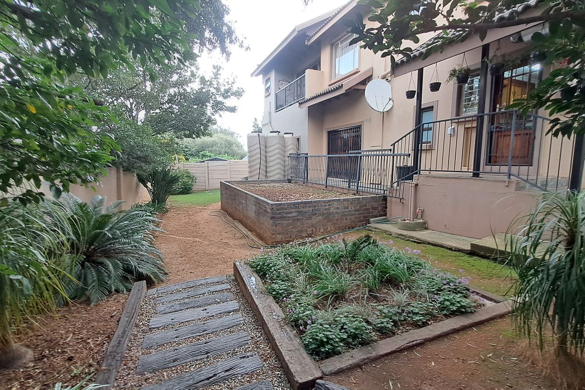Rear garden area featuring a raised brick planter, timber sleeper pathway, and established landscaping with boundary wall and water storage tanks.