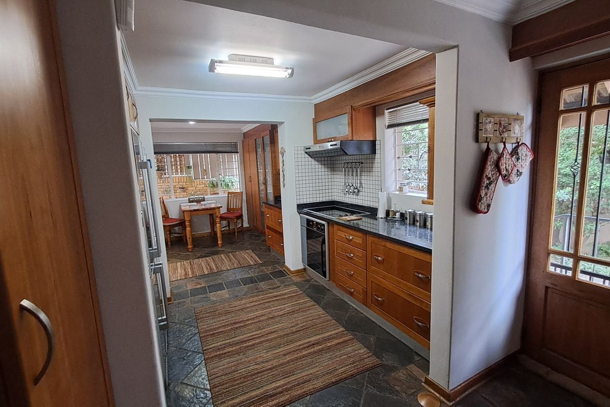 A functional kitchen featuring warm wooden cabinetry, granite countertops, built-in oven and hob, and durable slate tile flooring with direct access to the patio.