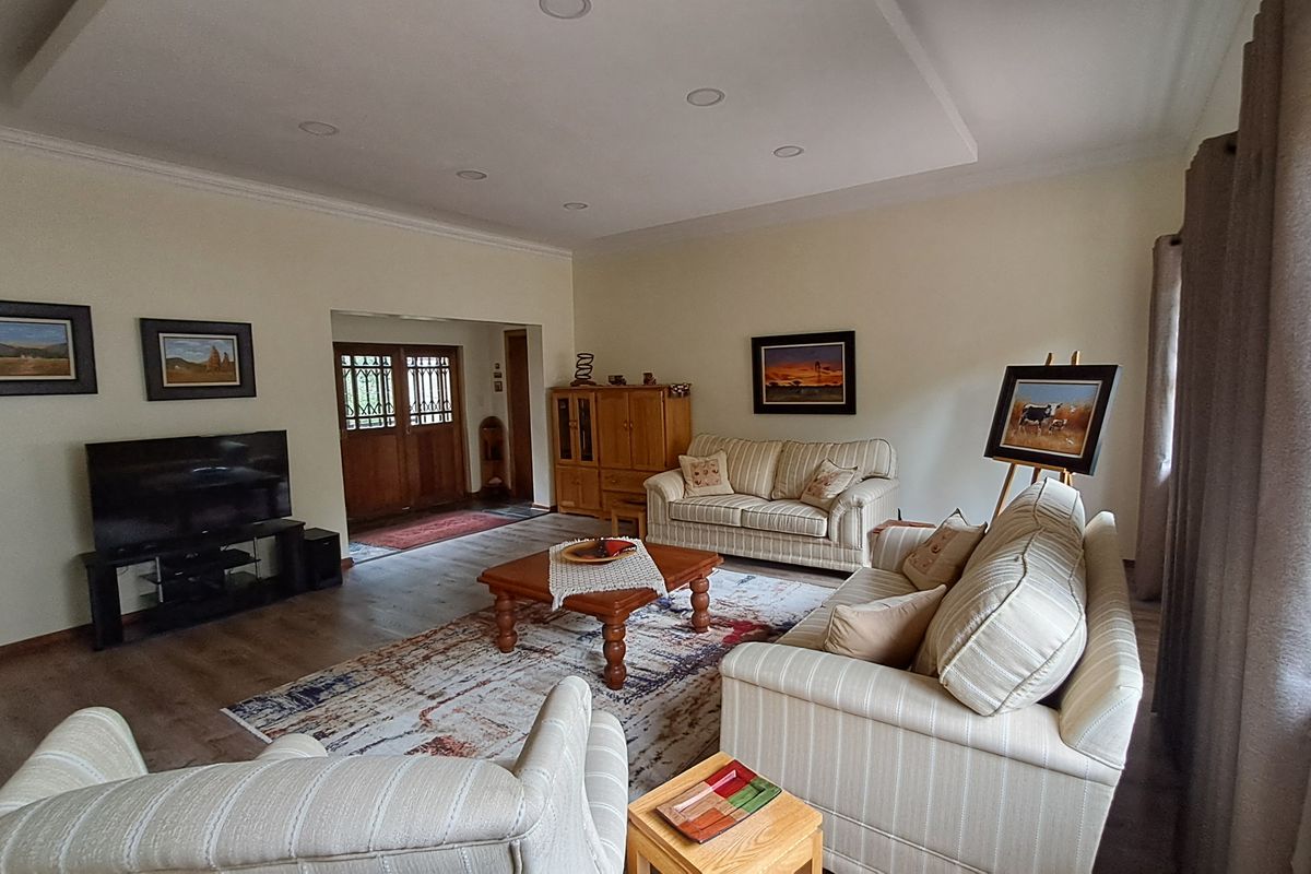 A spacious living room featuring recessed ceiling lighting, laminate flooring, and double wooden entrance doors, creating a comfortable and inviting atmosphere.
