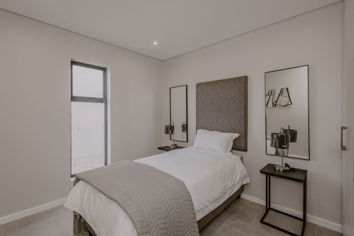 A modern, neutral-toned bedroom featuring tiled flooring, recessed lighting, and a built-in cupboard, offering a clean and functional living space.