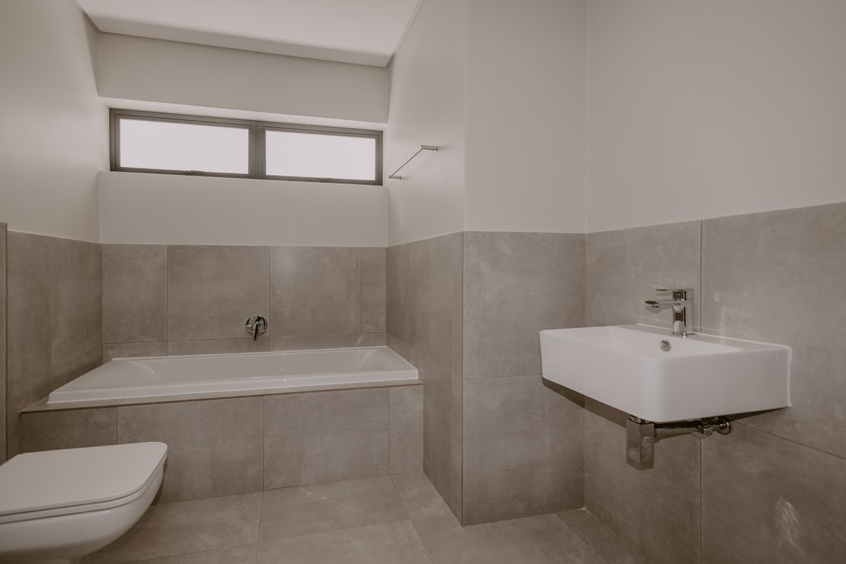 Modern bathroom featuring a built-in bathtub, wall-hung toilet, and wall-mounted basin with neutral grey tiling throughout.