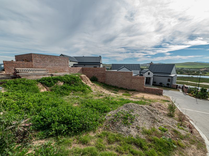 Exterior view of a modern house with brick boundary walls and a paved driveway, showing ongoing site development and landscaping.