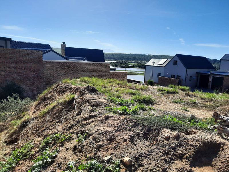 Rear view of the property showing an unlandscaped plot with a brick boundary wall and views of neighboring homes and the surrounding landscape.