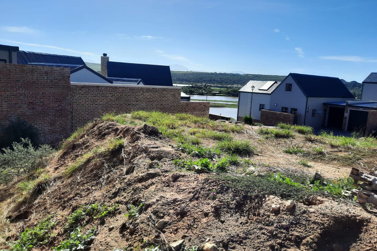 Rear view of the property showing an unlandscaped plot with a brick boundary wall and views of neighboring homes and the surrounding landscape.