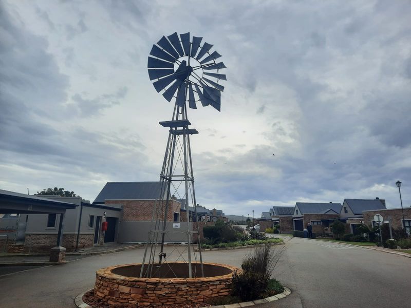 A view of the residential estate entrance featuring a decorative windmill and stone-clad planter set within a paved driveway area.