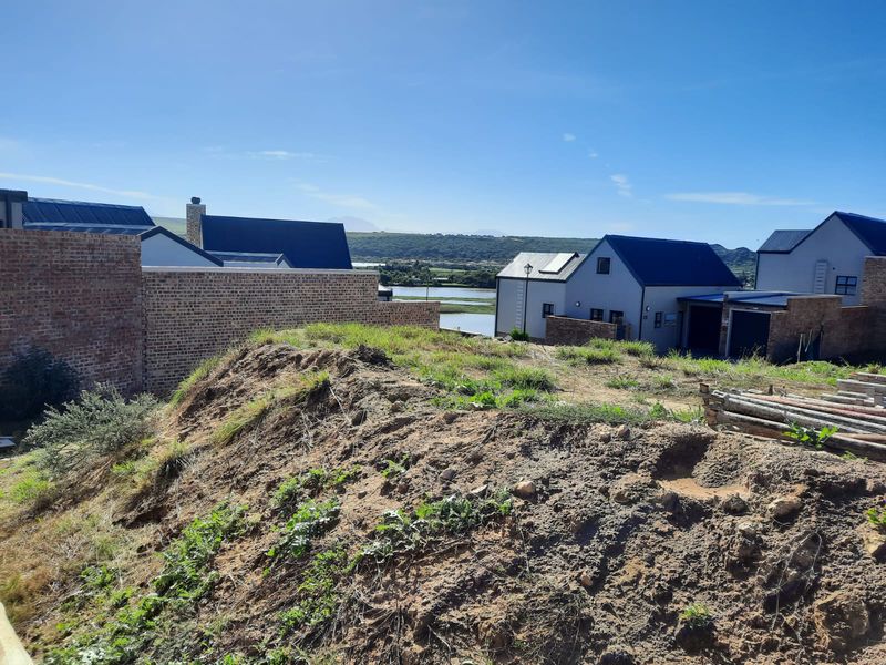 Elevated view overlooking a residential estate with modern homes, brick boundary walls, and a distant water feature under a clear blue sky.