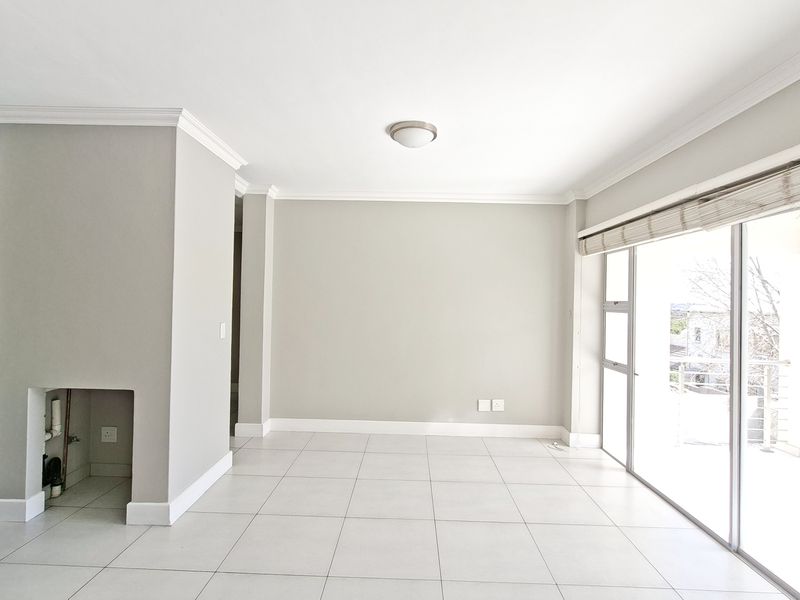 Bright open-plan living area featuring tiled floors, crown molding, and direct access to a balcony, with an adjacent kitchen area.