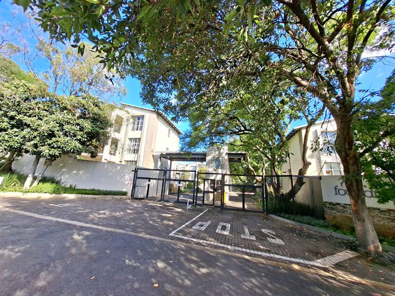 Front entrance view of the apartment complex featuring a secure gated access point, paved driveway, and established trees.