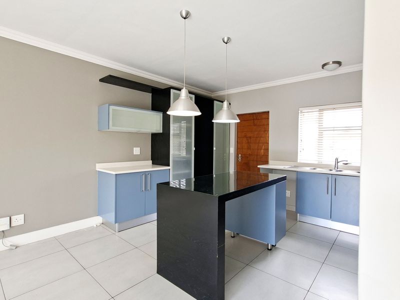 Modern kitchen featuring blue cabinetry, a central black island, stone countertops, and tiled flooring, offering a clean and functional workspace.