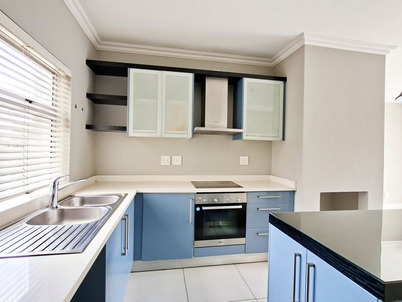 Modern kitchen featuring blue cabinetry, stone countertops, integrated stainless steel appliances, and tiled flooring with ample natural light.
