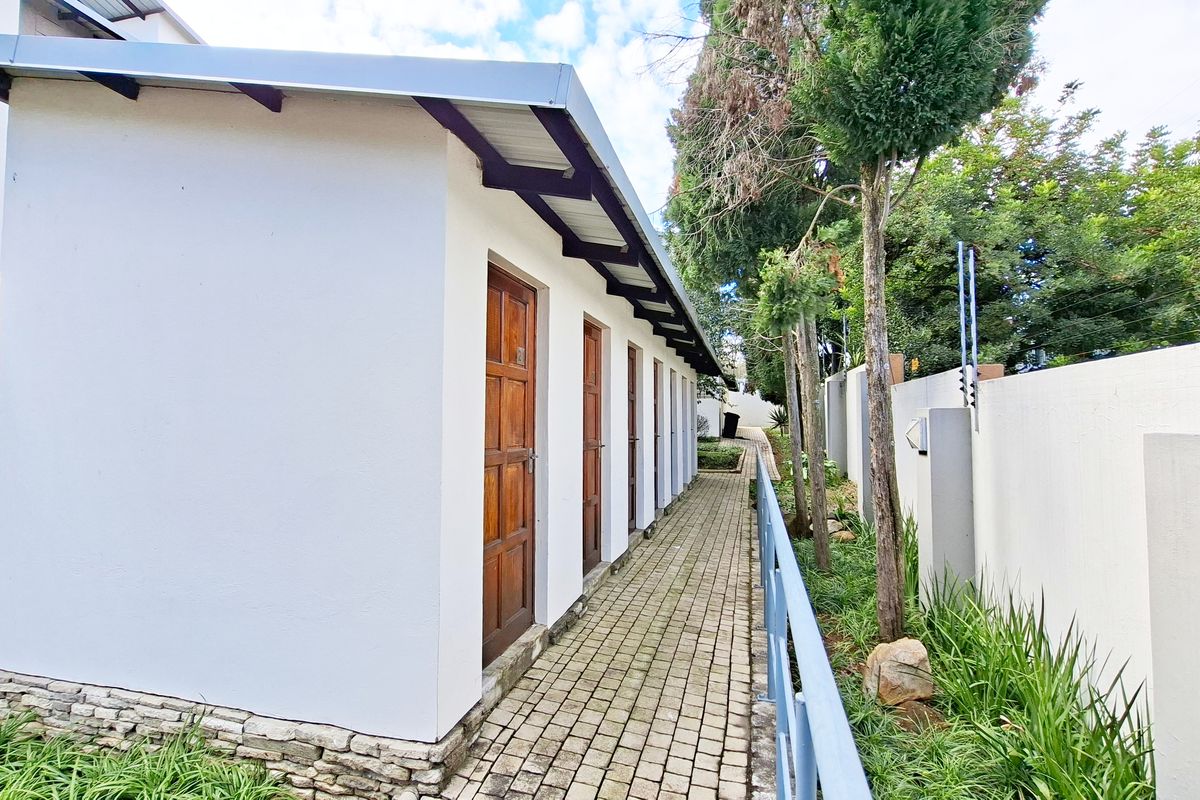 A paved exterior walkway alongside a building structure featuring multiple wooden doors, stone base detailing, and secure perimeter walling with electric fencing.