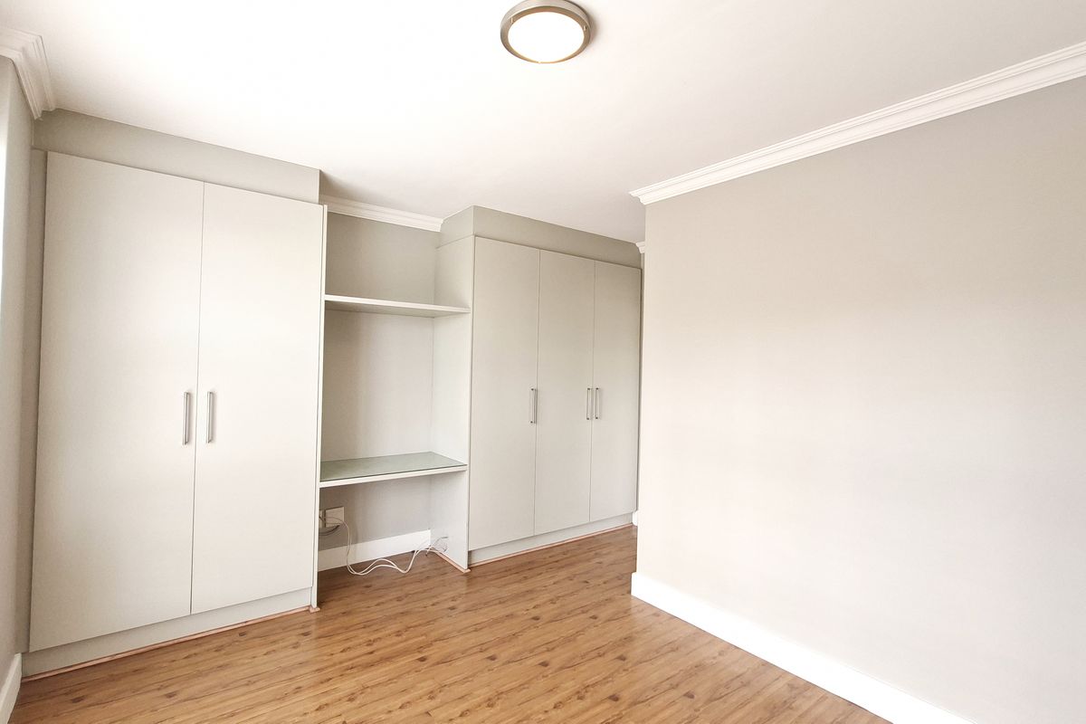 A bright, empty bedroom featuring neutral walls, laminate flooring, and extensive built-in cabinetry with an integrated desk area.
