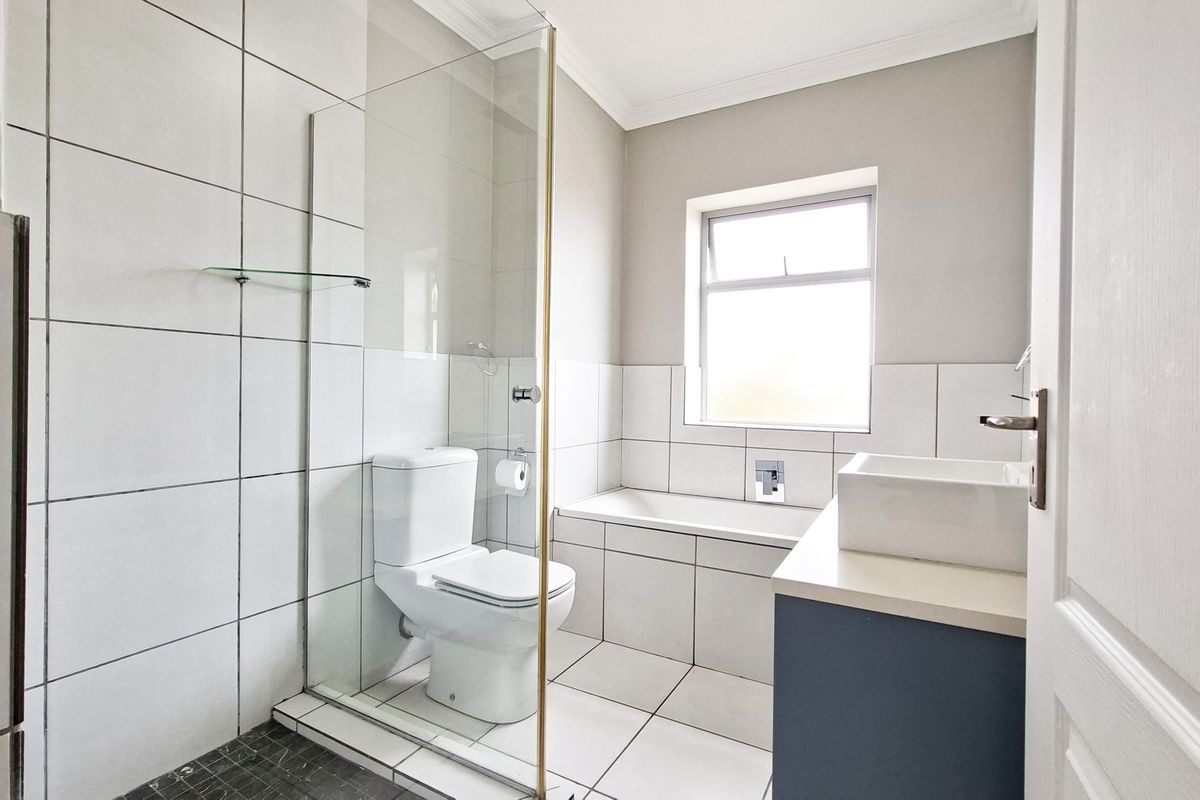 A clean, modern bathroom featuring a glass-enclosed shower, a built-in bathtub, and a vanity unit with a basin.