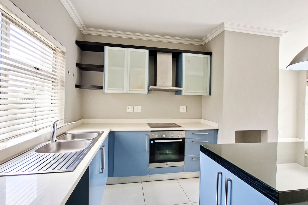 Modern kitchen featuring blue cabinetry, stone countertops, integrated stainless steel appliances, and tiled flooring with ample natural light.