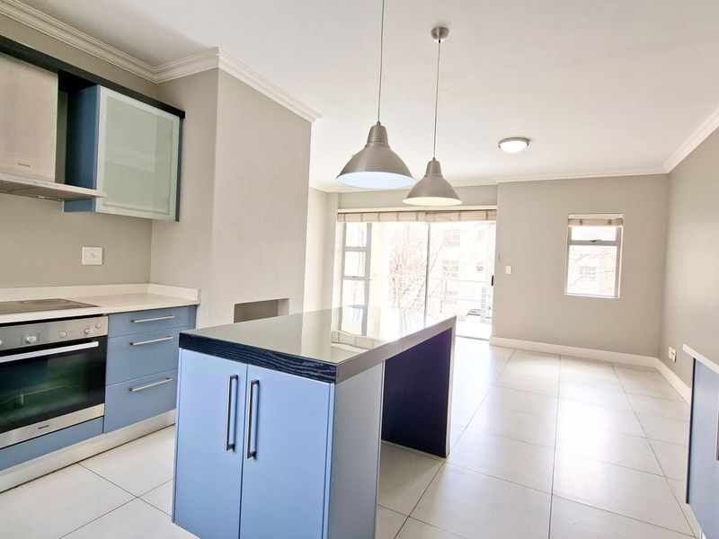Modern open-plan kitchen and living area featuring blue cabinetry, stone countertops, built-in appliances, and tiled flooring leading to a balcony.