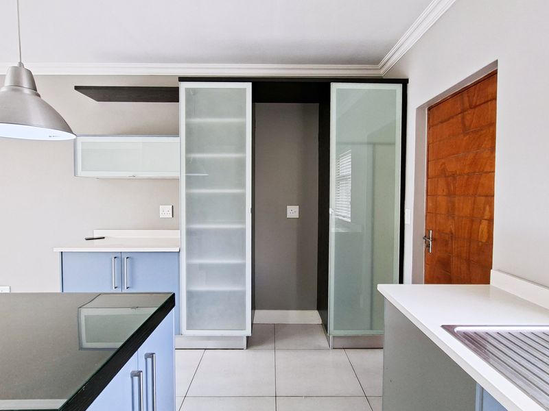 Modern kitchen featuring light blue cabinetry, frosted glass pantry doors, stone countertops, and a stainless steel sink, offering a clean and functional workspace.