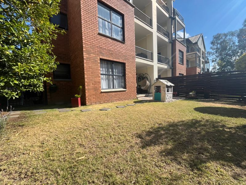 Rear view of a brick apartment building featuring a private lawn area, timber fencing, and upper-level balconies with metal railings.
