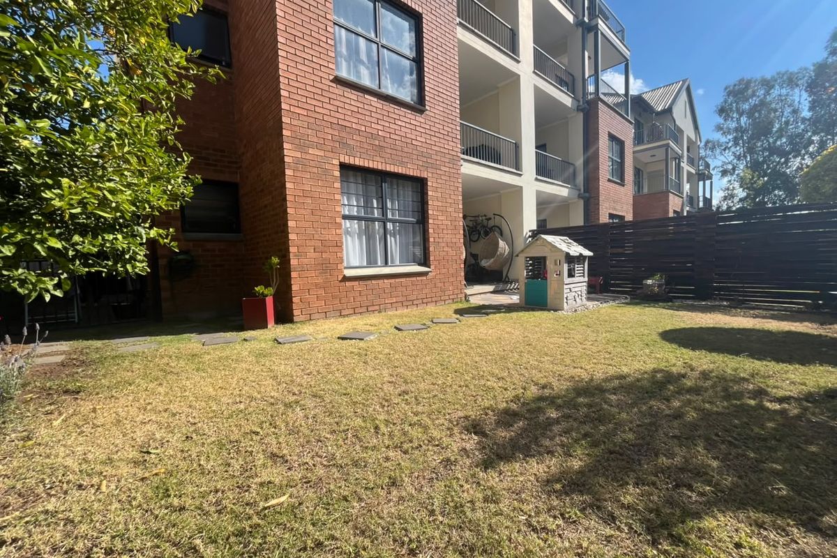 Rear view of a brick apartment building featuring a private lawn area, timber fencing, and upper-level balconies with metal railings.