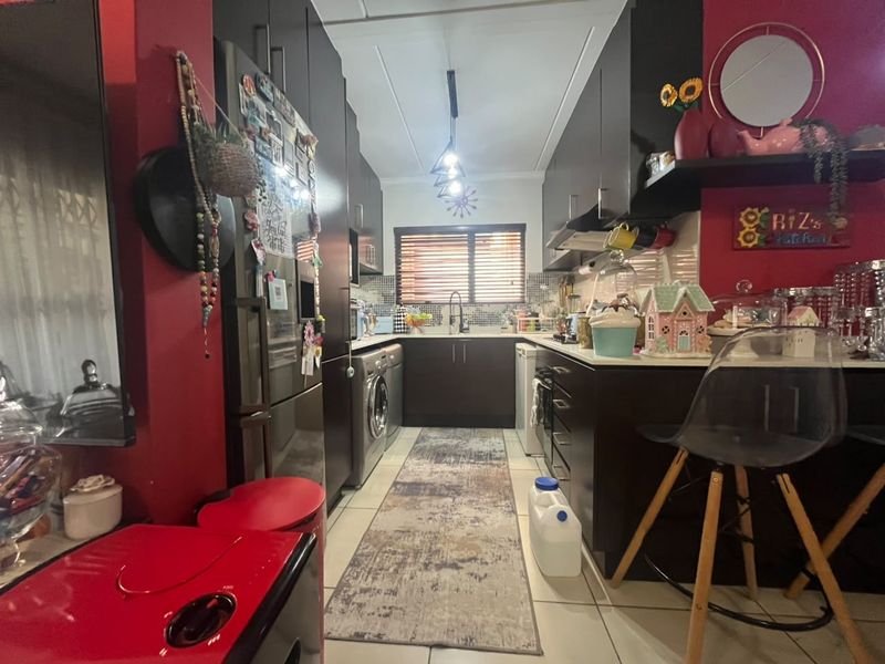 A compact kitchen featuring dark cabinetry, tiled flooring, and integrated appliances, offering a functional layout with a modern aesthetic.