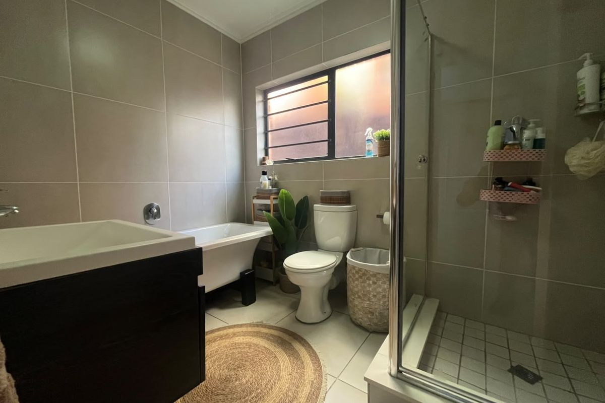 A well-maintained bathroom featuring a freestanding bathtub, a separate glass-enclosed shower, a vanity cabinet, and neutral wall tiling.