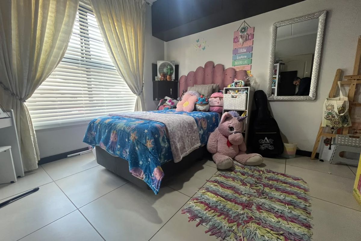 A well-maintained bedroom featuring tiled flooring, built-in cupboards, and large windows fitted with venetian blinds and curtains, providing ample natural light.