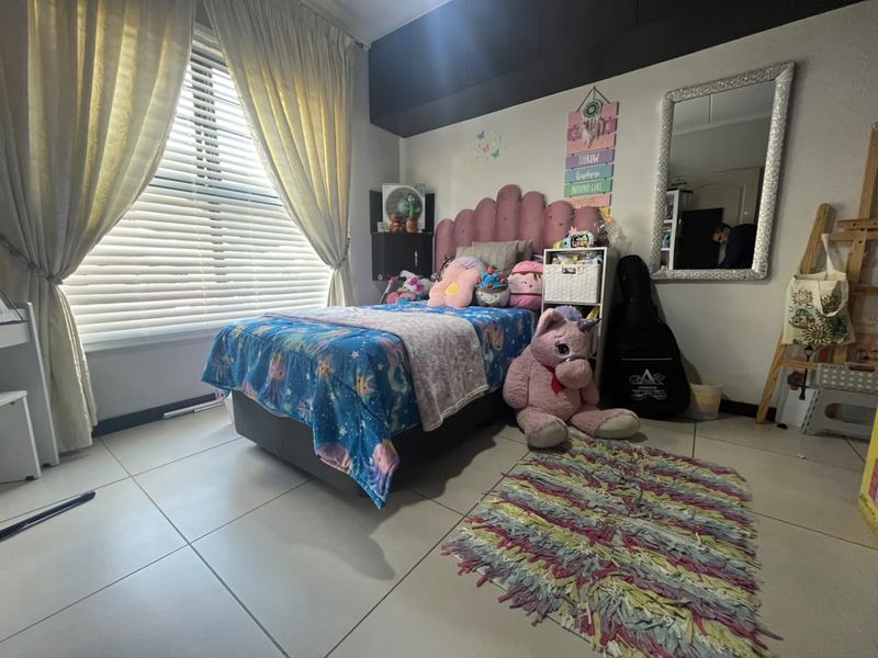 A well-maintained bedroom featuring tiled flooring, built-in cupboards, and large windows fitted with venetian blinds and curtains, providing ample natural light.
