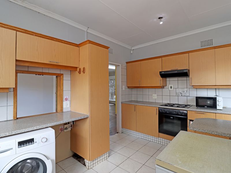 Functional kitchen featuring light wood cabinetry, laminate countertops, tiled backsplash, and integrated appliances including an oven, hob, and extractor fan.