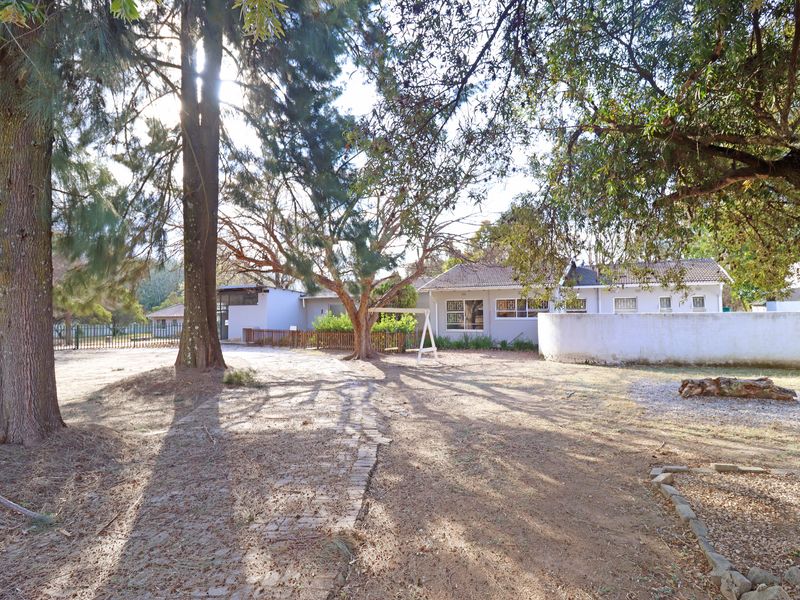 A spacious rear garden area featuring mature trees, a brick paved pathway, and a view of the rear building elevation with a tiled roof.