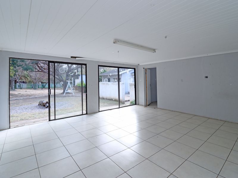 Spacious, empty living area featuring white tiled flooring, tongue and groove ceiling, and large sliding glass doors providing direct access to the garden.