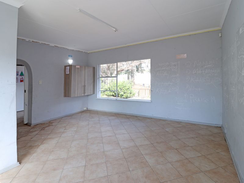 An empty living room featuring tiled flooring, a wall-mounted cabinet, and an archway entrance, currently requiring cosmetic repairs and repainting.