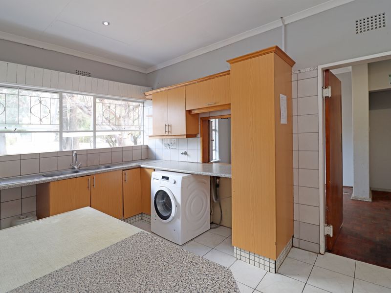 Functional laundry room featuring laminate cabinetry, tiled splashbacks, stainless steel sink, and tiled flooring with direct access to adjacent living areas.