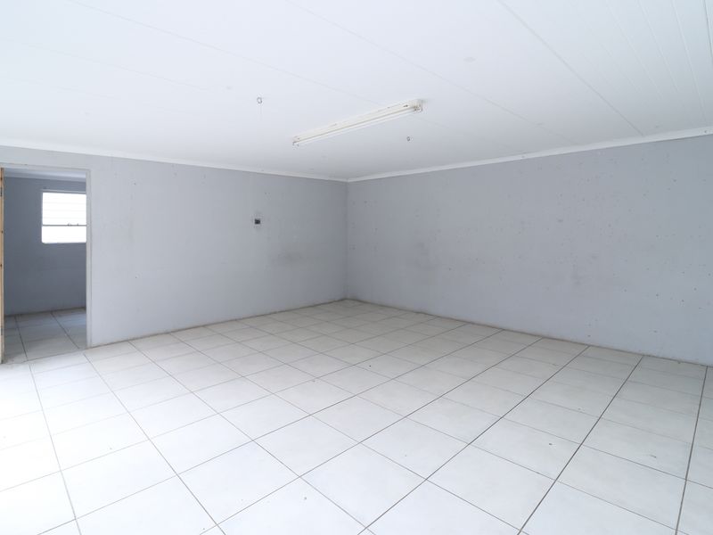 An empty, neutral-toned living area featuring tiled flooring and a simple ceiling light fixture, offering a blank canvas for renovation.