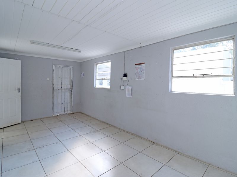 An empty, utilitarian room featuring tiled flooring, timber panel ceiling, and security-fitted doors and windows, suitable for a home office or utility space.