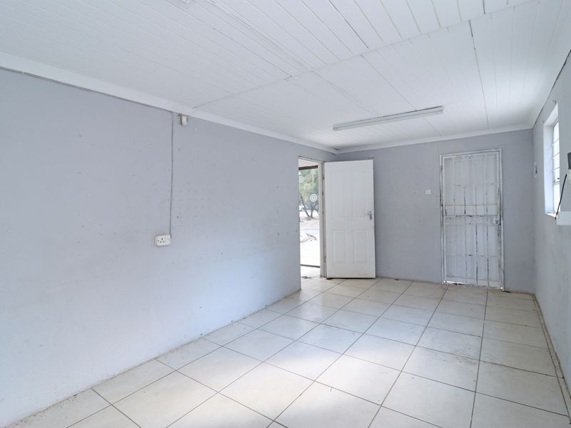 An empty, neutrally painted living area featuring tiled flooring, a timber panel ceiling, and a security gate leading to the exterior.