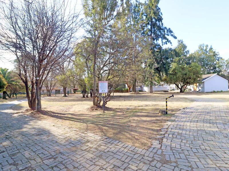 A spacious outdoor garden area featuring a paved driveway, mature trees, and perimeter fencing, offering a natural setting for the property.