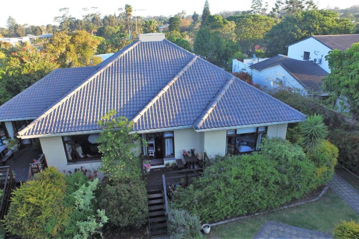 Aerial view of a residential property featuring a tiled roof, surrounding garden, and timber decking with access stairs.