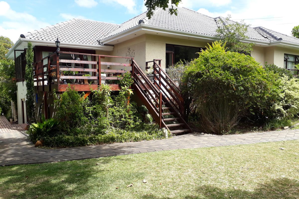 Rear view of the property featuring a raised timber deck with stairs leading down to a paved walkway and landscaped garden area.