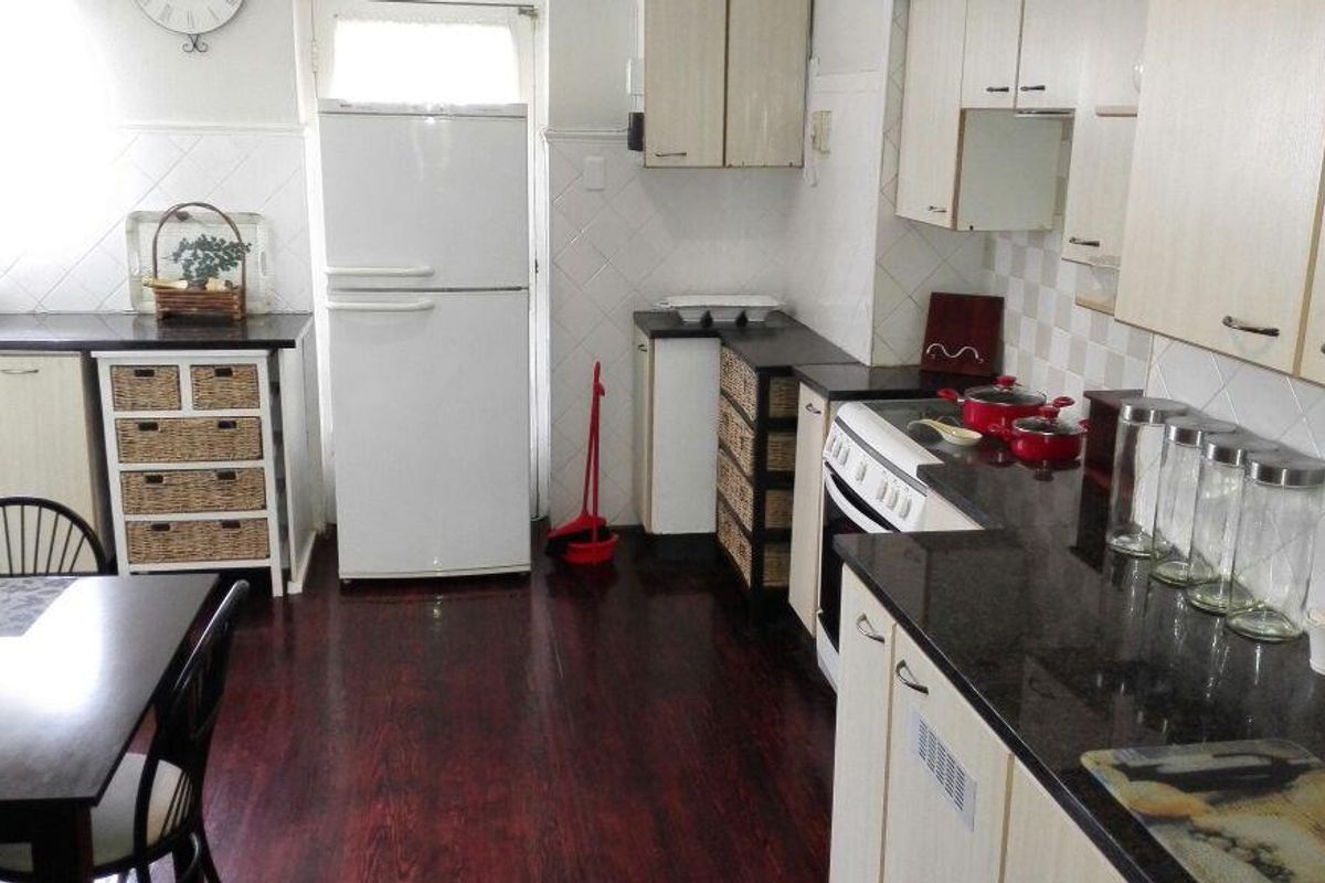 A functional kitchen featuring dark granite countertops, light-toned cabinetry, tiled backsplash, and dark laminate flooring, offering a practical layout for daily meal preparation.