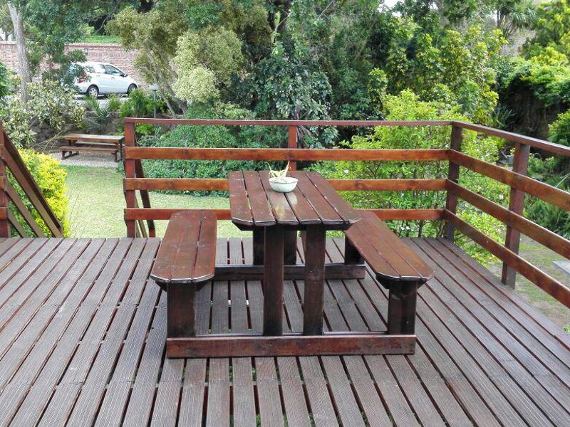 An elevated timber deck featuring a wooden balustrade and staircase, overlooking a lush garden area.