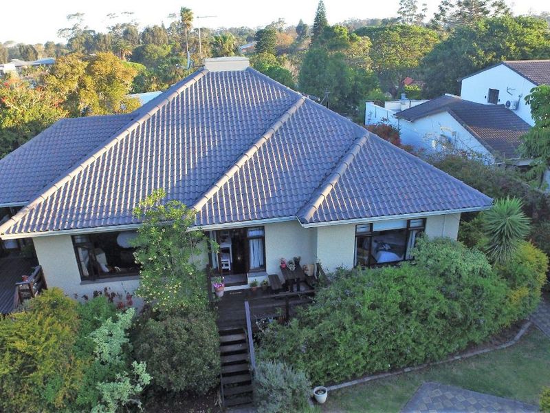 Aerial view of a residential property featuring a tiled roof, surrounding garden, and timber decking with access stairs.