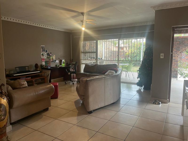 Spacious living room featuring tiled flooring, crown molding, a ceiling fan, and large sliding glass doors providing access to the outdoor area.