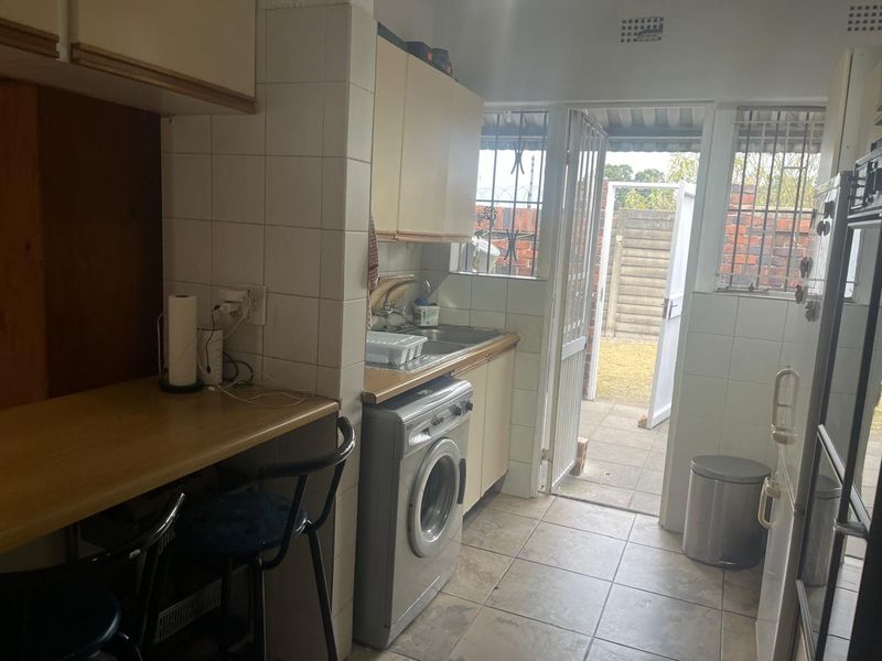 A functional kitchen area featuring built-in cabinetry, tiled splashbacks, and direct access to the rear exterior through a security gate.
