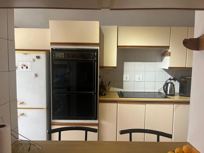A functional kitchen featuring built-in oven, electric cooktop, tiled backsplash, and ample cabinetry, offering a dated aesthetic ready for modern updates.