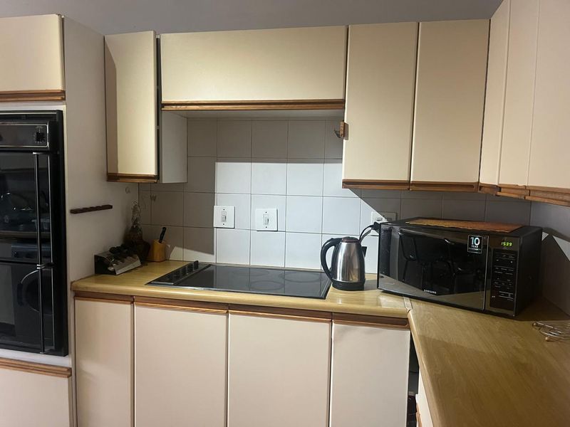 A functional kitchen featuring built-in oven, electric cooktop, laminate countertops, and tiled backsplash with ample cabinetry for storage.
