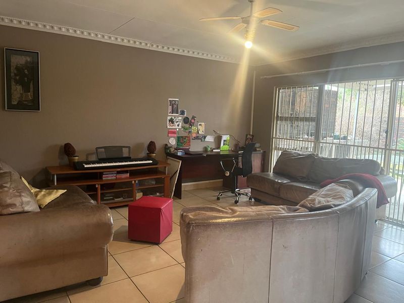 Spacious living room featuring tiled flooring, decorative ceiling cornices, a ceiling fan, and large sliding glass doors leading to the exterior.