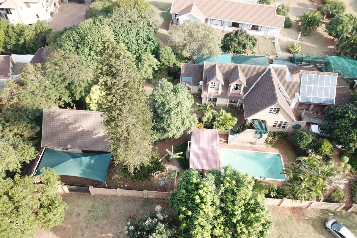 Aerial view of a residential property featuring a swimming pool, solar panels, mature garden, and multiple roof structures.