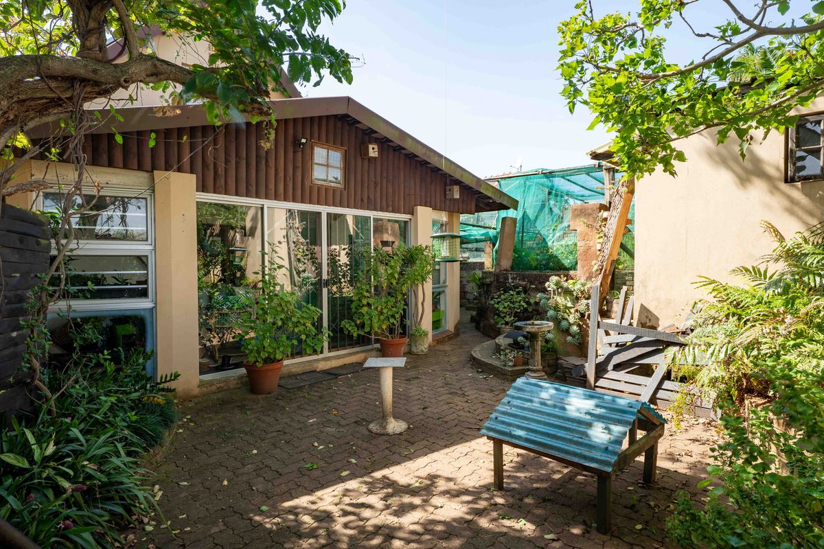 A rear garden area featuring a paved patio, timber-clad exterior wall, and large sliding glass doors providing access to the home.