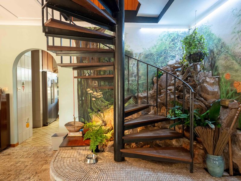 A unique interior hallway featuring a central spiral staircase, stone feature wall with mural, and arched access to the kitchen area.